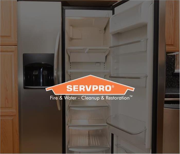 stainless steel fridge with the right side open and empty in the middle of wooden cabinets with the SERVPRO logo over the top