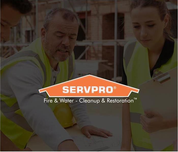 a reconstruction team that includes 3 males and one female in yellow vests looking at plans for a building. SERVPRO logo is o